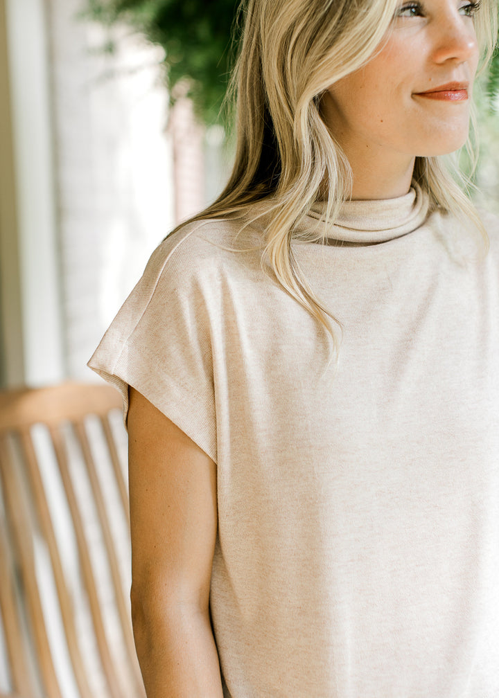 Model wearing an oatmeal lightweight sweater with extended sleeves and a mock neck.  