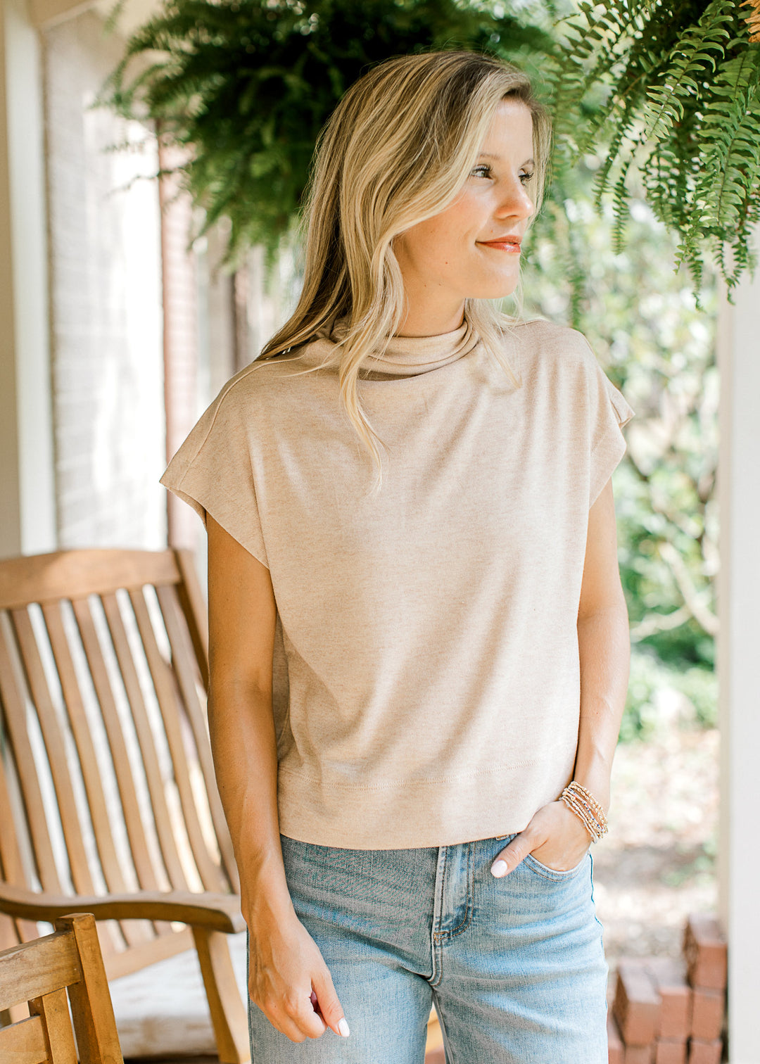Model wearing jeans and an oatmeal lightweight sweater with extended sleeves and a mock neck.  