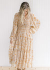 Model wearing a taupe fully lined maxi with a yellow and light brown floral pattern and long sleeves
