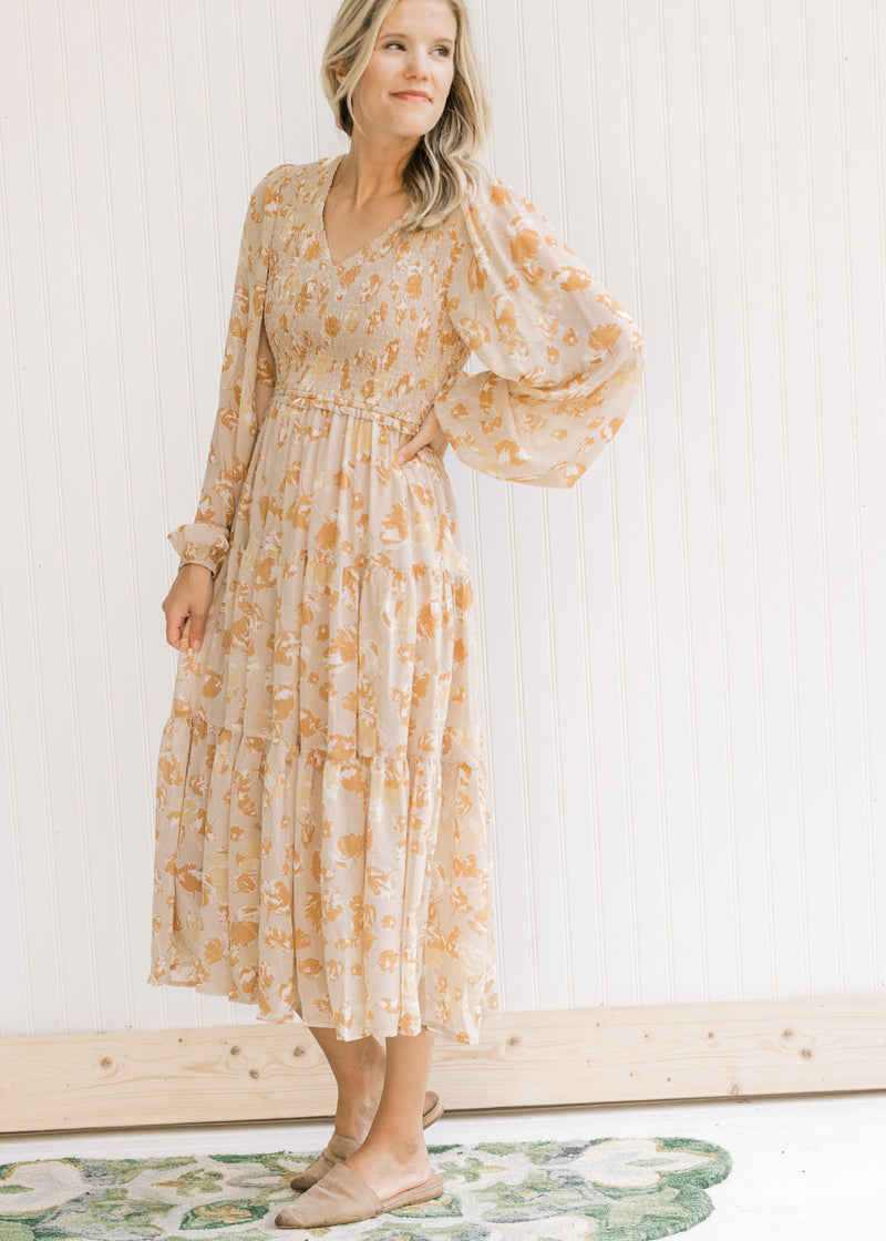 Model wearing flat mules with a taupe long sleeve maxi with a yellow and light brown floral pattern.