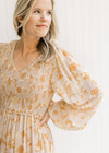 Close up of smocked bodice, v-neck and sheer long sleeves on a taupe maxi with a floral pattern. 