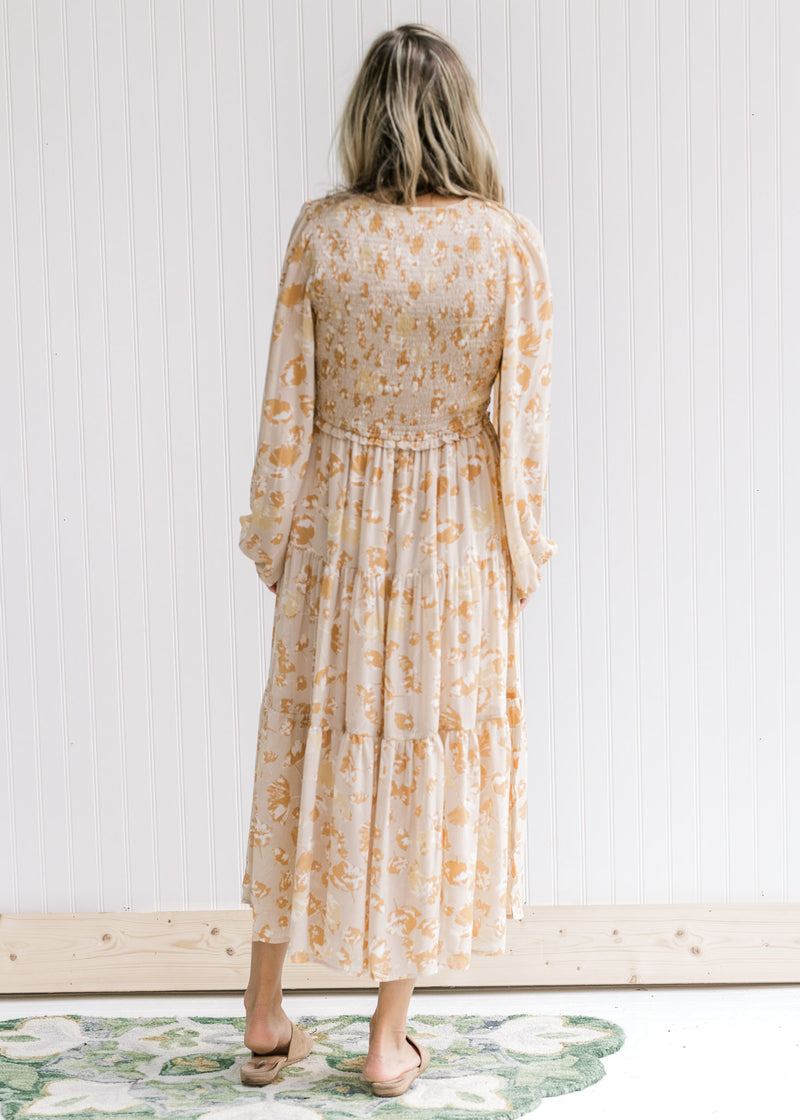 Back view of model wearing a taupe long sleeve maxi with a yellow and light brown floral pattern.