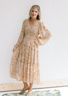Model wearing a taupe maxi with a yellow and light brown floral pattern and sheer long sleeves. 