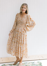 Model wearing a taupe maxi with a yellow and light brown floral pattern and sheer long sleeves. 