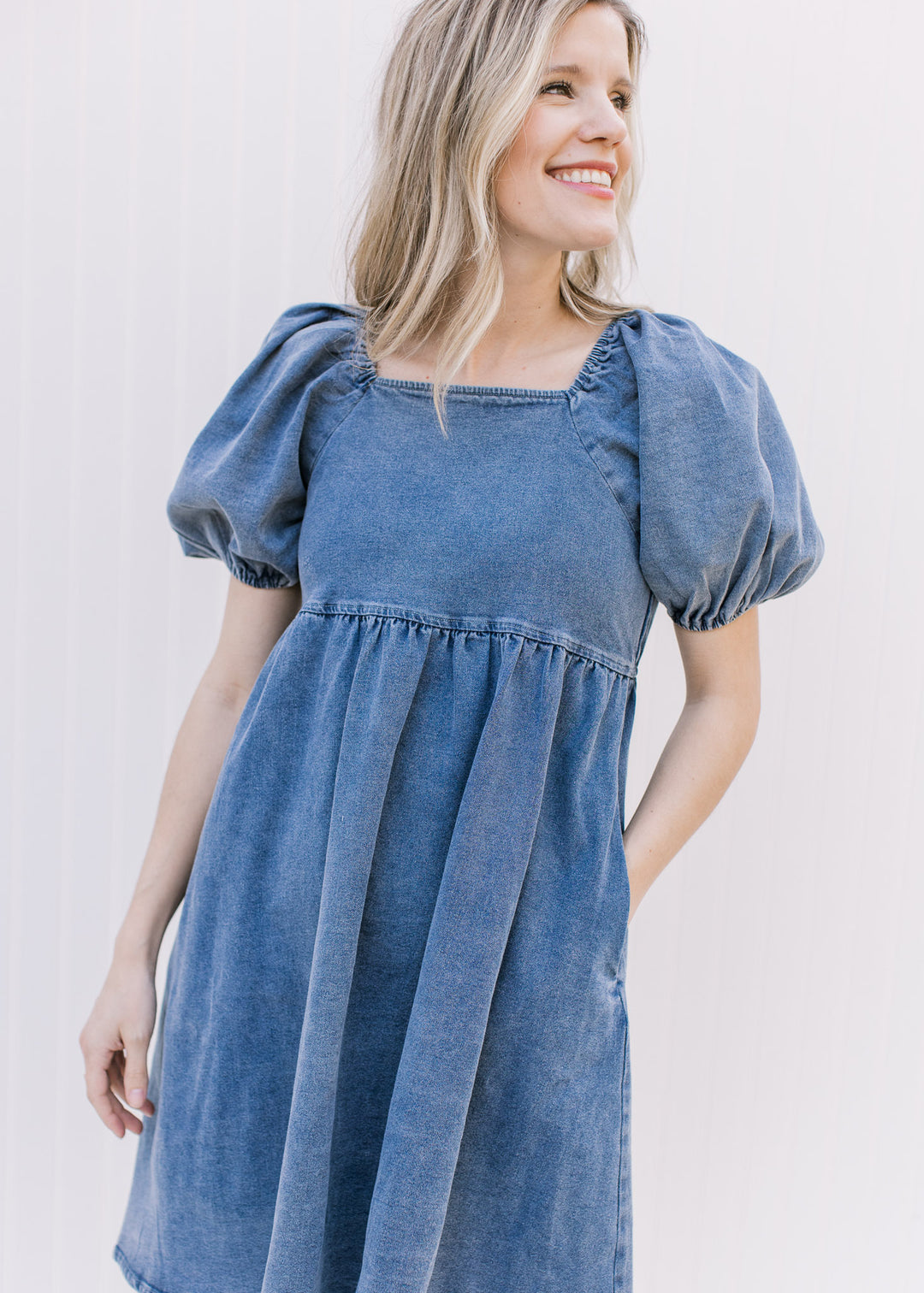 Model wearing a medium washed denim dress with bubble short sleeves and a square neck.