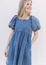 Model wearing a medium washed denim dress with bubble short sleeves and a square neck.