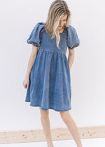 Model wearing a medium washed above the knee denim dress with short sleeves and a square neck.