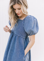 Close up of Model wearing a medium washed denim dress with bubble short sleeves and a square neck.
