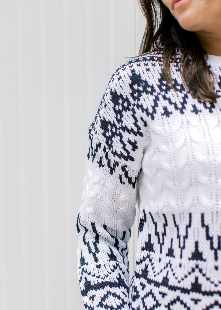 Close up of navy fair isle pattern on a cream sweater with a round neckline and long sleeves. 
