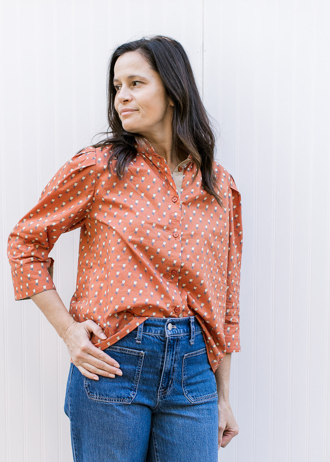 Model wearing a rust top with soft yellow floral print, ruffle neck and 3/4 sleeve with button cuff.