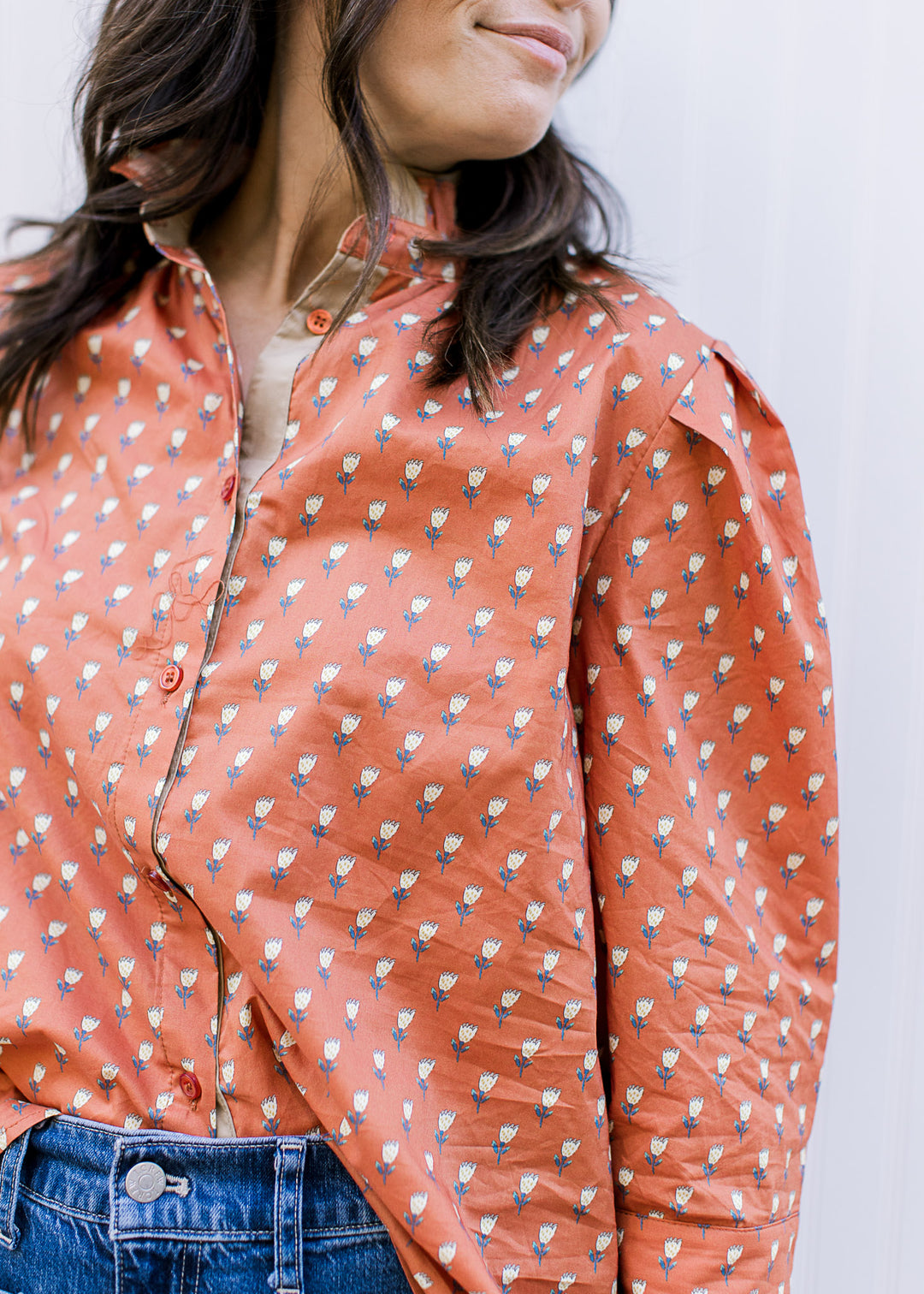 Close up of pleated shoulder and button front on a rust colored top with soft yellow floral print. 