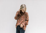 Model wearing a rust top with a cream floral, sheer poet long sleeves and a mock neck. 