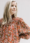 Close up of mock neckline with a smocked yolk on a rust long sleeve top with a cream floral. 