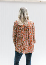 Back view of Model wearing a rust long sleeve top with a cream floral a mock neck with smocked yolk.