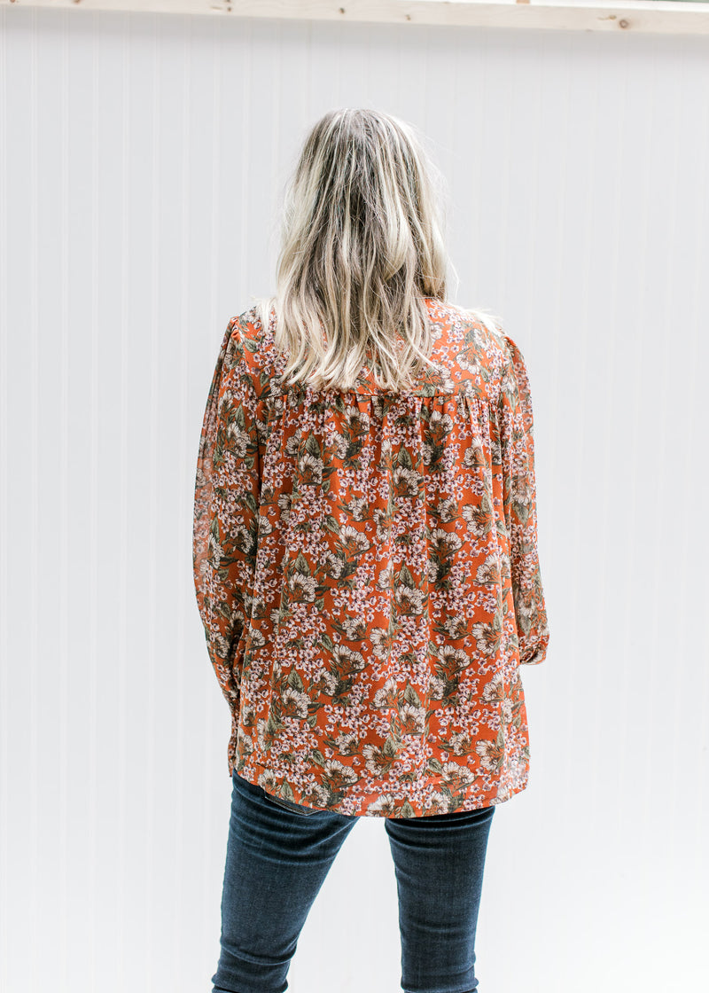 Back view of Model wearing a rust long sleeve top with a cream floral a mock neck with smocked yolk.