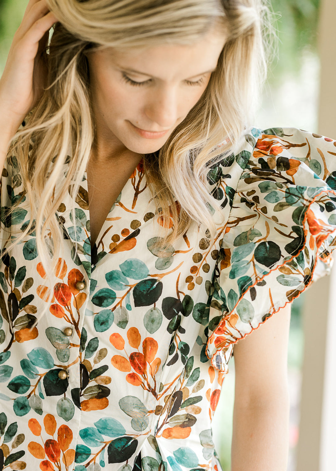 Close up of v-neck with a collar, layered cap sleeves and three gold buttons on a cream midi.