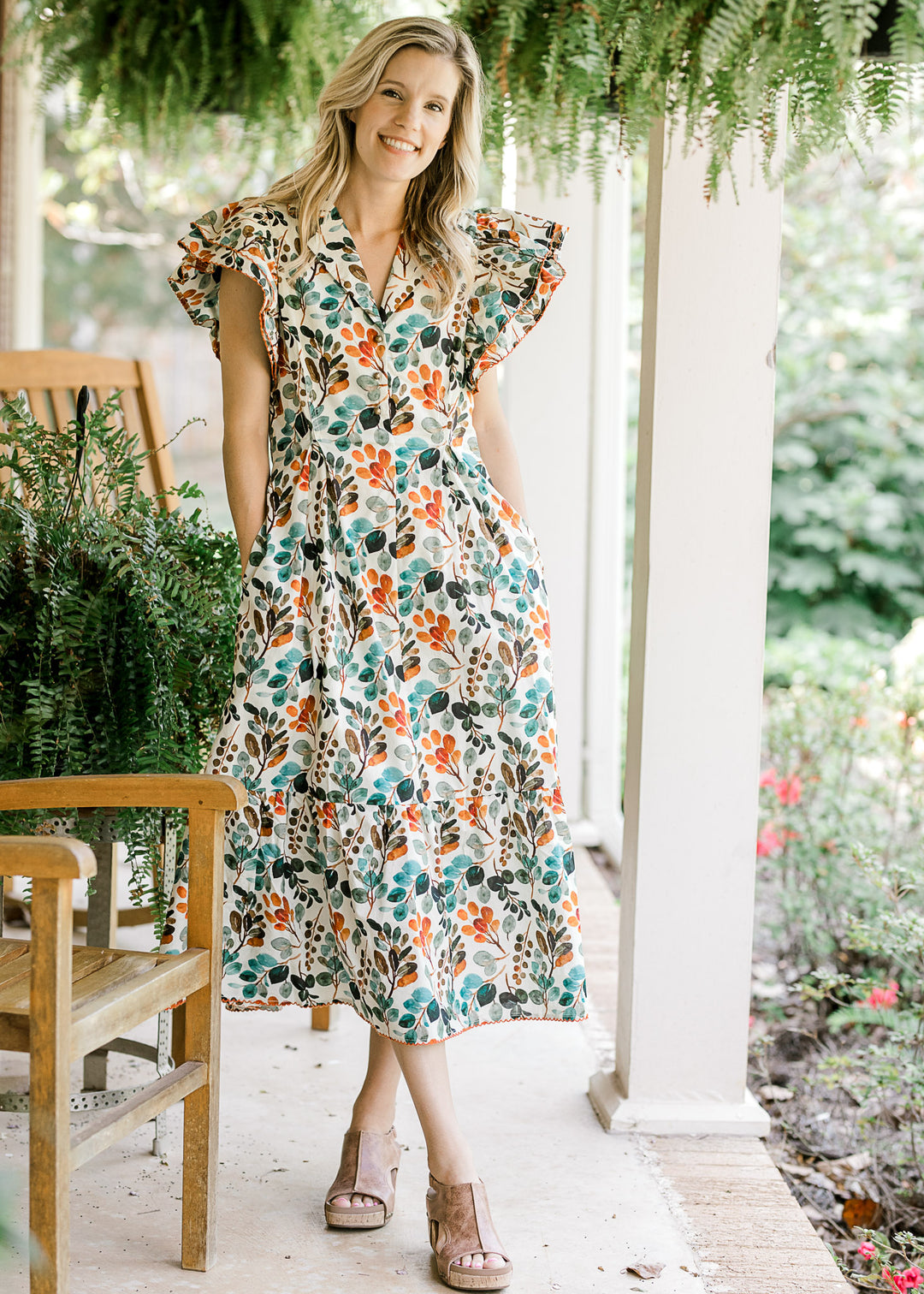 Model wearing a cream midi with fall floral, layered flutter cap sleeves, pockets and a v-neck. 