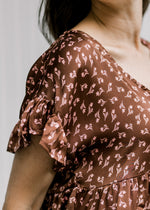 Close up of rust v-neck top with pink floral and short sleeves with a ruffle and a babydoll fit. 