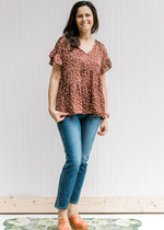 Model wearing mules and jeans with a rust top with light pink floral pattern and short sleeves. 