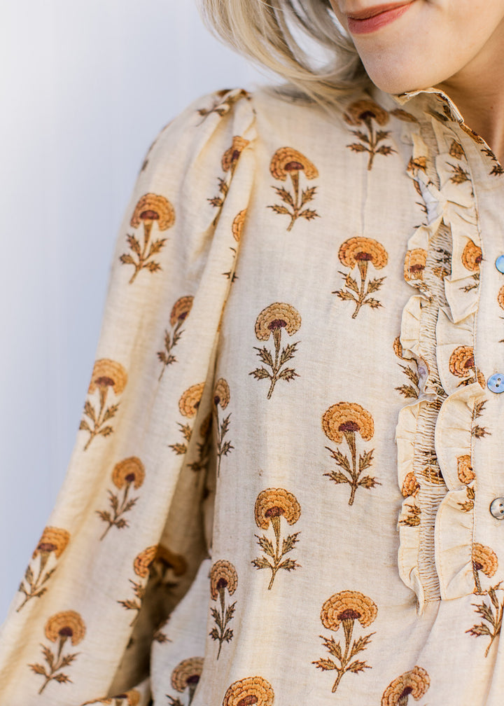 Close up of ruffle placket and pleated shoulder on a camel colored top with mustard floral. 