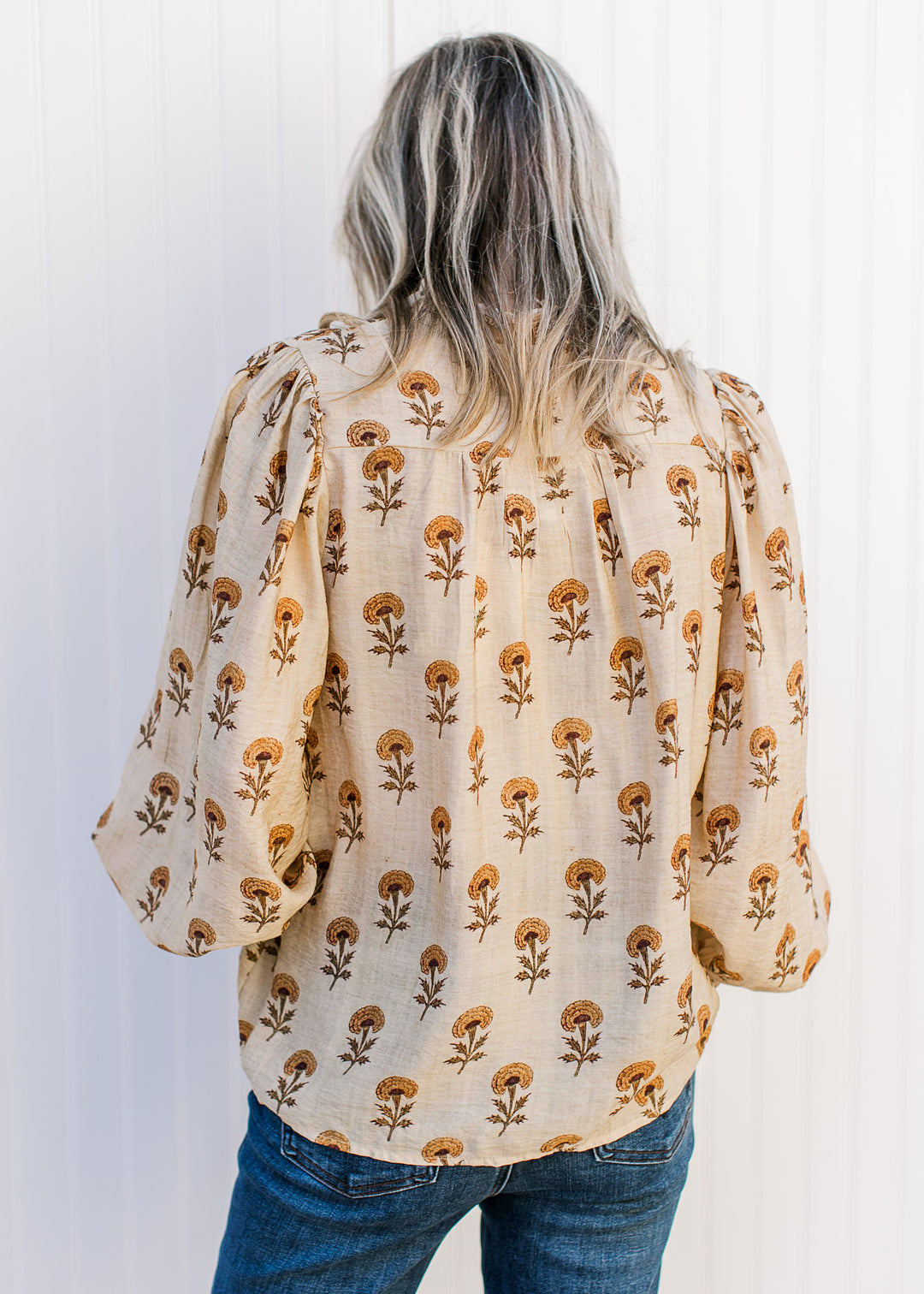 Back view of Model wearing a camel top with mustard floral, button placket and poet long sleeves.