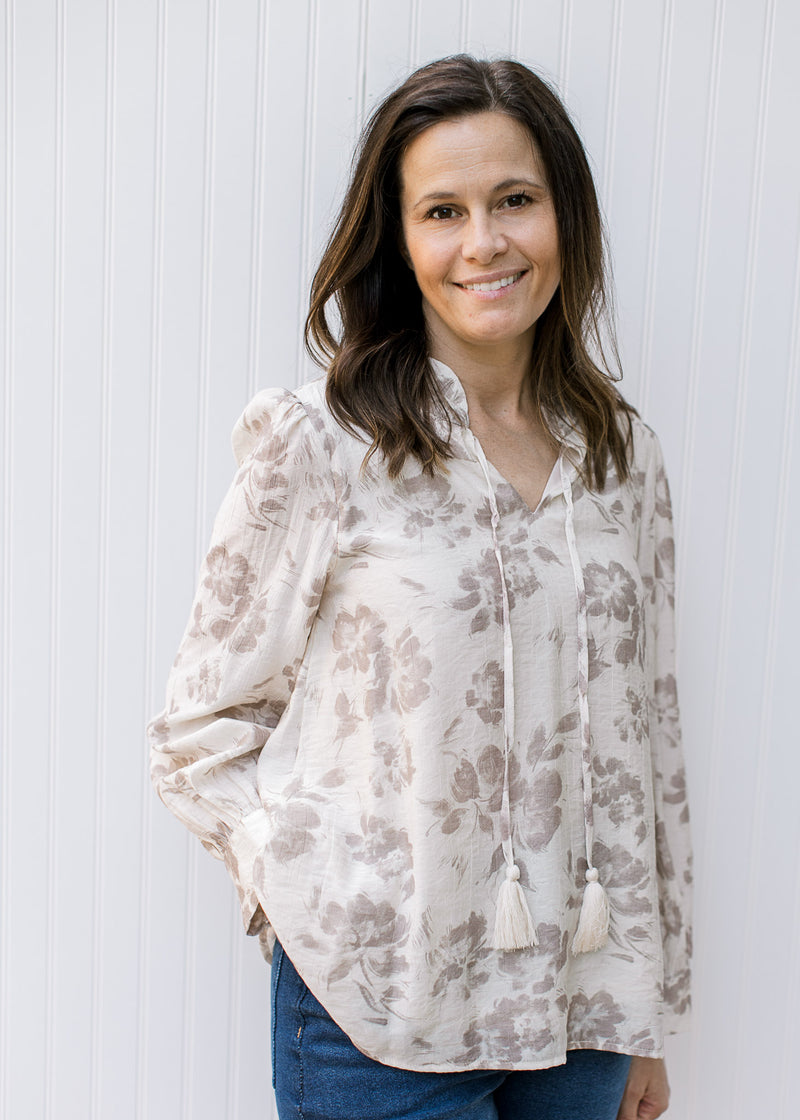 Model wearing a cream top with taupe flowers, v-neck with a tie and long sleeves. 