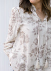 Close up of v-neck with a tie on a cream top with taupe flowers and long sleeves. 