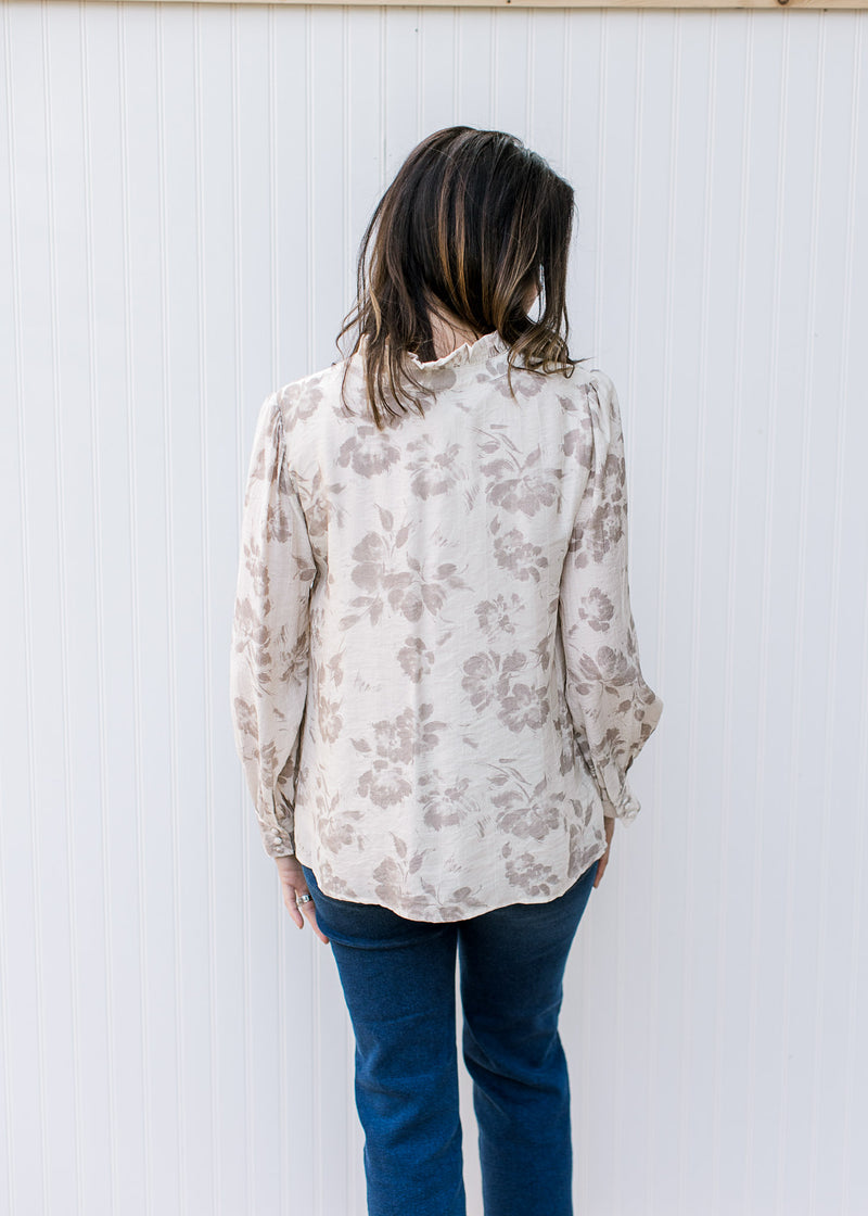 Back view of Model wearing a cream top with taupe flowers, v-neck with a tie and long sleeves. 