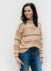 Model wearing a textured sweater striped with fall colors having long sleeves and a round neck. 