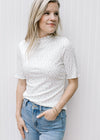 Model wearing a ribbed cream floral top with a ruffle at short sleeve, hem and mock neck.