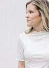 Close up of model wearing a cream fitted top with ditsy floral, and ruffle sleeve and neck. 