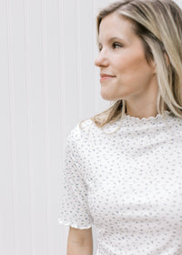 Close up of model wearing a cream fitted top with ditsy floral, and ruffle sleeve and neck. 