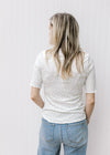 Back view of Model wearing a cream floral top with a ruffle at short sleeve, hem and mock neck.