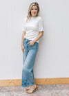 Model wearing jeans and a ribbed cream floral top with a ruffle at short sleeve, hem and mock neck.