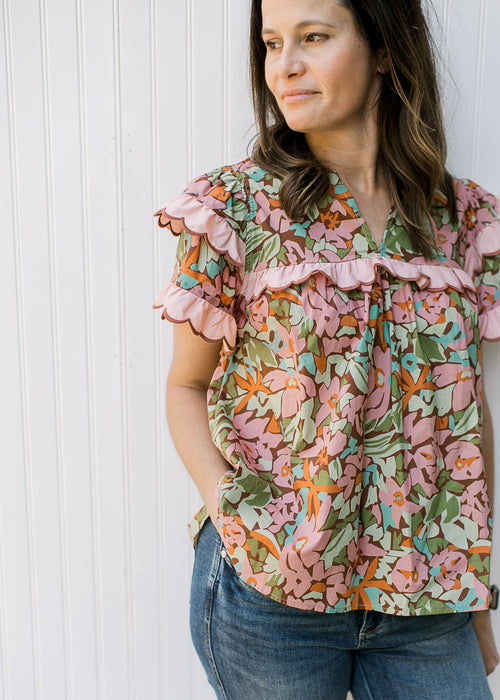 Model wearing a brown short sleeve top with a floral design and pink ruffle at yolk and sleeves.