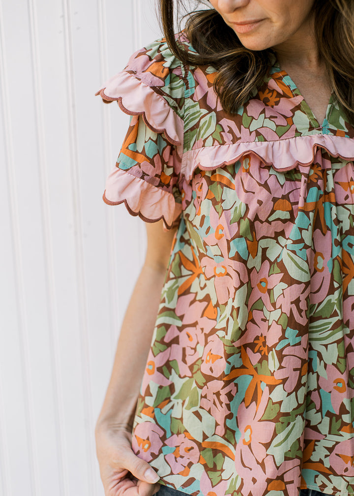 Close up of pink ruffle at yolk and sleeves on a v-neck brown top with bright flowers. 