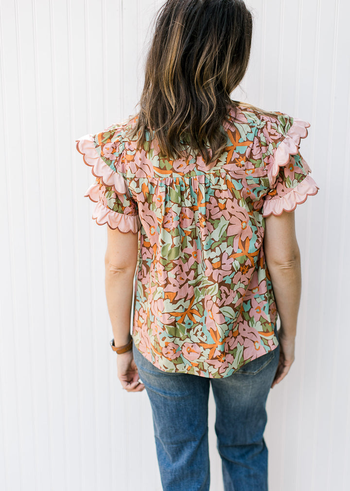 Back view of model wearing a brown top with bright flowers, short sleeves and ruffles. 