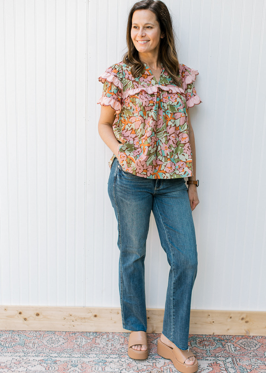 Model wearing jeans with a brown short sleeve top with bright flowers and short sleeves. 