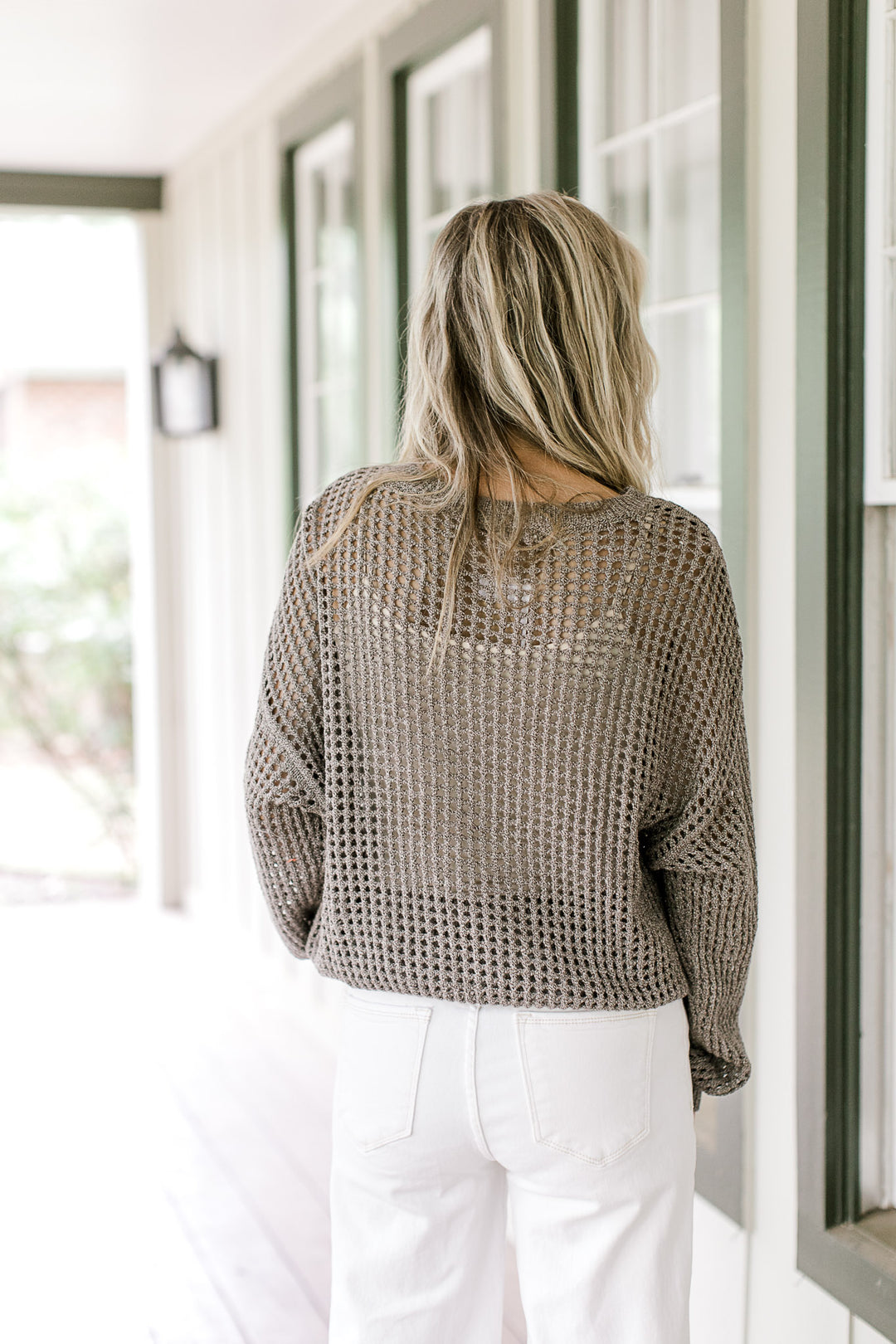 Back view of Model wearing a brown loose knit sweater with long sleeves and a round neck.