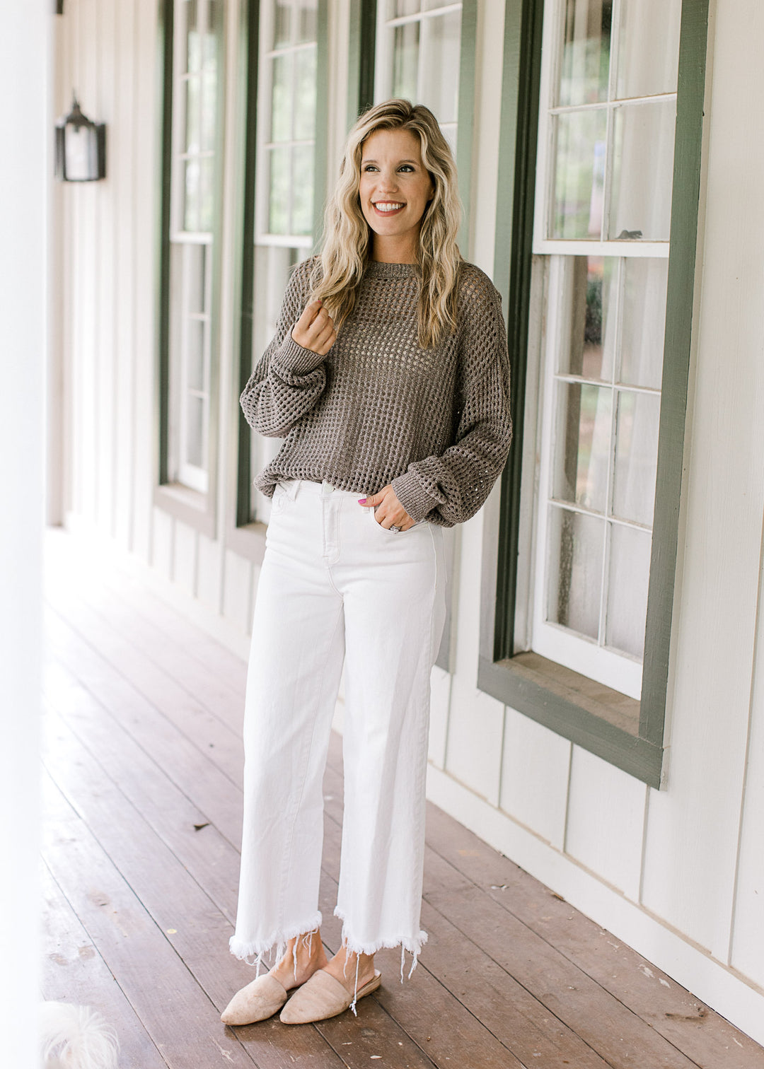 Model wearing mules, white jeans and a brown loose knit sweater with long sleeves and a round neck.