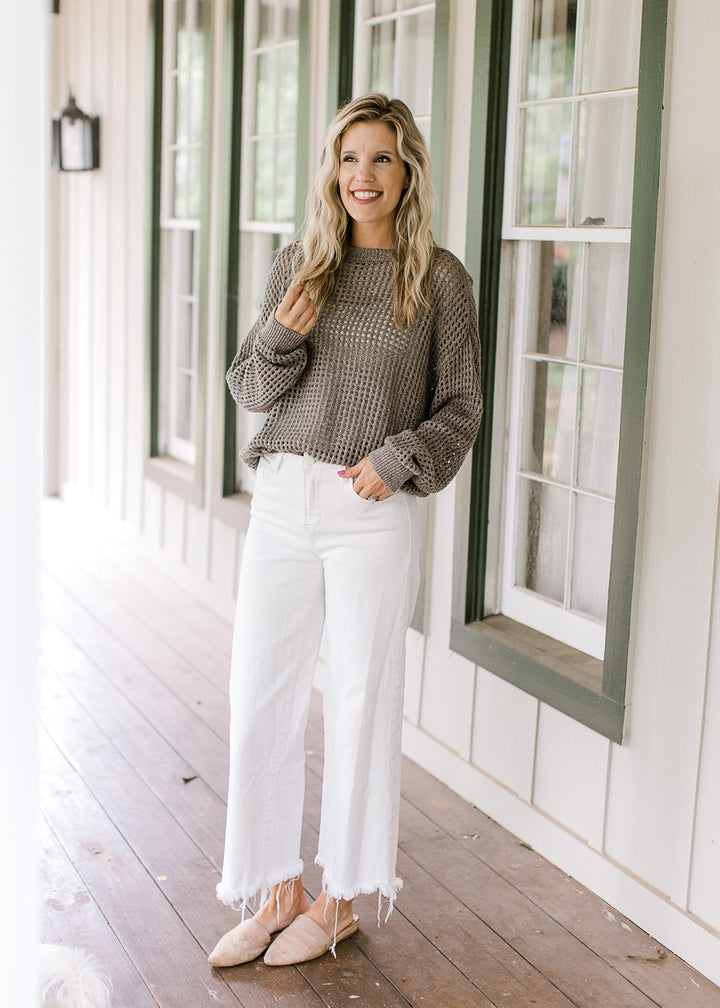 Model wearing mules, white jeans and a brown loose knit sweater with long sleeves and a round neck.