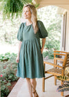 Model wearing a deep sage, gauze dress hitting just above the knees with bubble short sleeves.