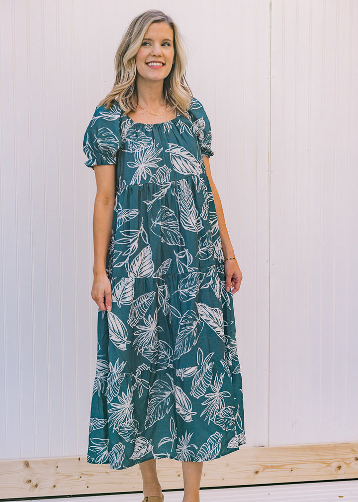 Model wearing a square neck turquoise midi dress with a cream floral pattern and short sleeves.