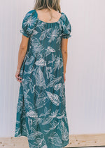 Back view of Model wearing a turquoise midi dress with a cream floral pattern and a square neck.