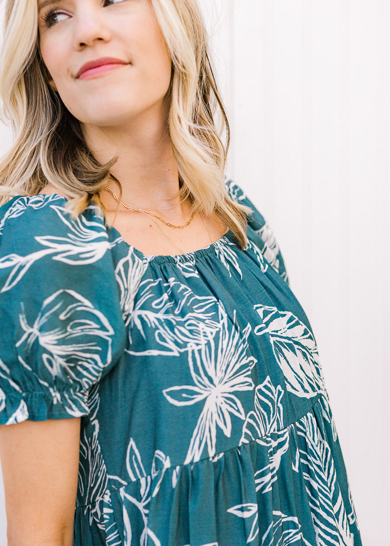 Close up view of square neckline and bubble short sleeves on a turquoise dress with cream floral. 