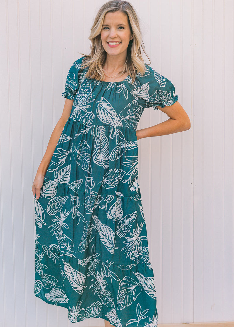 Model wearing a turquoise midi dress with a cream floral pattern, square neck and short sleeves.