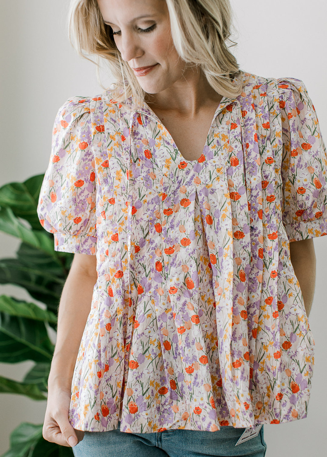 Model wearing an off-white top with floral print, v-neck with tie, pleated torso and short sleeves. 