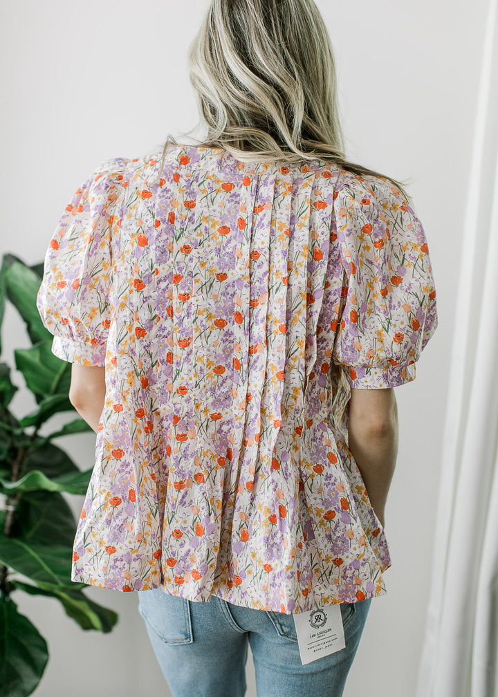 Back view of Model wearing an off-white top with floral print, pleated torso and short sleeves. 