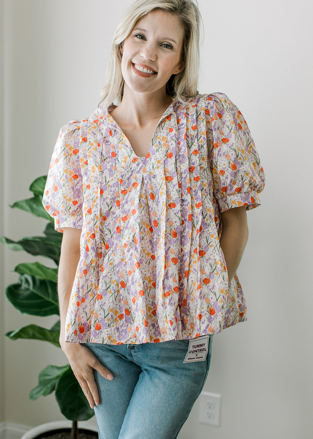 Model wearing jeans and an off-white top with floral print, v-neck, pleated torso and short sleeves.