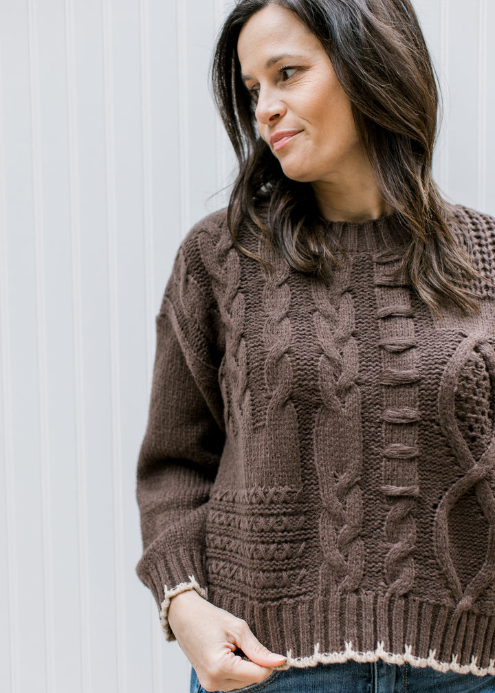 Close up of textured chunky knit on a brown sweater with tan stitching at hem and cuffs.